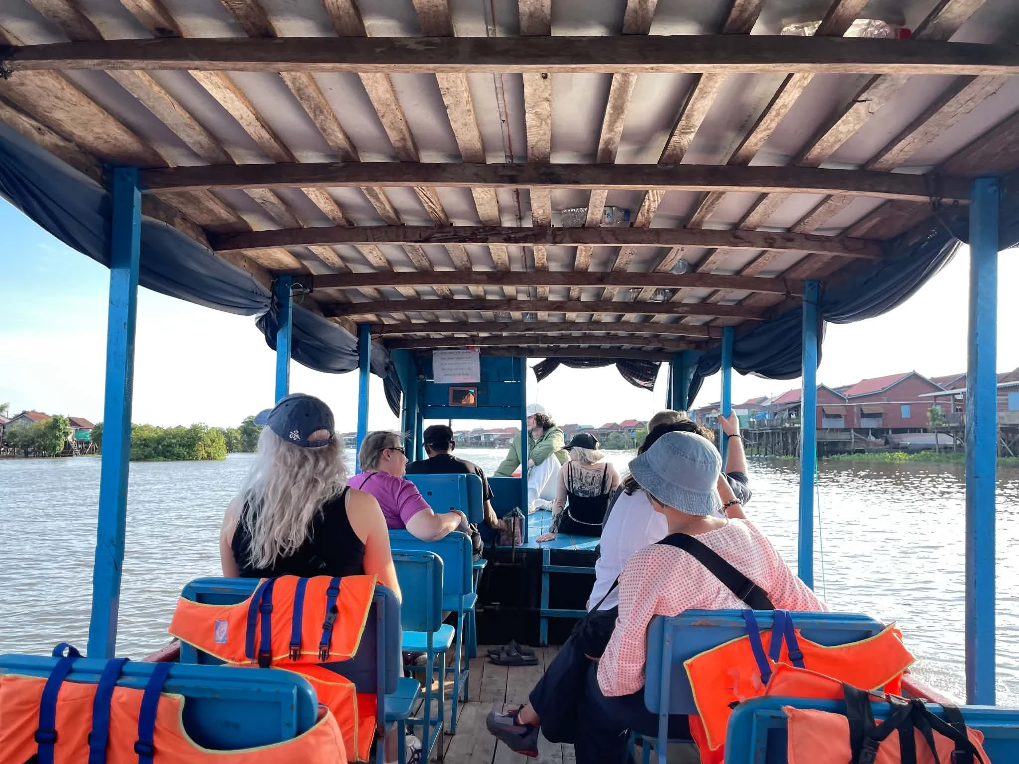 Guests on the covered village boat heading into Kompong Khleang, stilt houses along the right bank