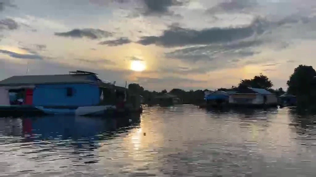 A blue floating house on Tonle Sap Lake with the sun setting behind broken cloud
