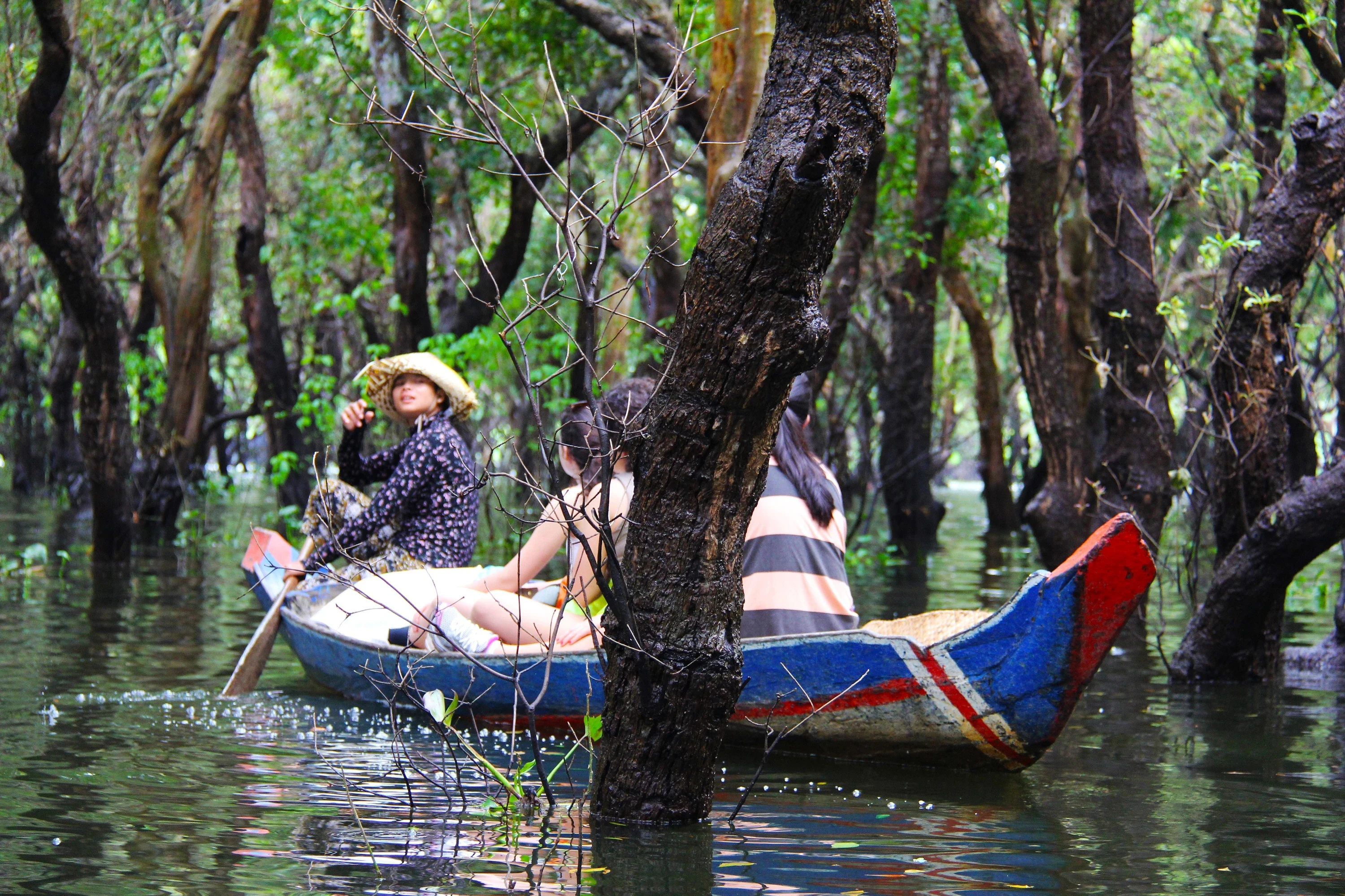 Two women paddle a canoe between flooded trees at Kompong Phluk